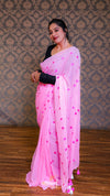 Woman wearing a pink saree with heart patterns against a patterned wall.