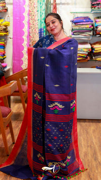 Woman holding a blue saree with red border in a fabric store.