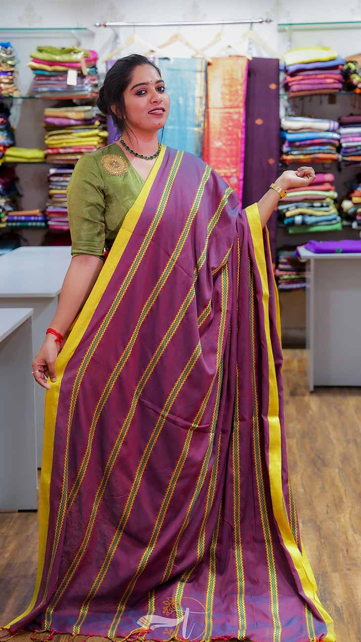 Woman wearing a purple saree with yellow stripes in a fabric store.