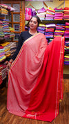 Woman holding a pink saree with a red border in a fabric store.