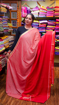 Woman holding a pink saree with a red border in a fabric store.