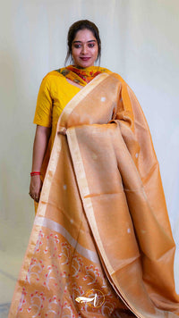 Woman wearing a yellow saree with a white blouse against a plain background