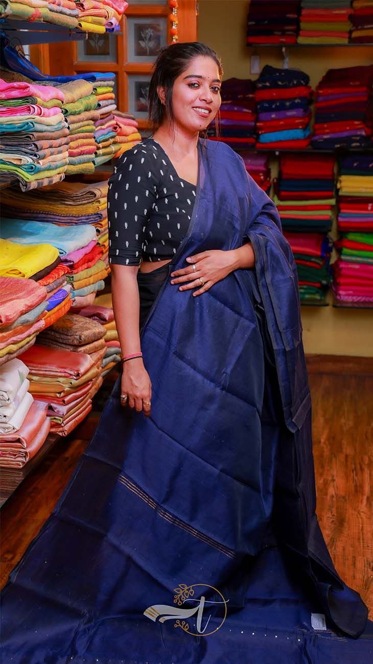 Woman in a blue saree standing in a fabric store with colorful fabrics in the background