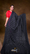 Woman wearing a black saree with white checkered pattern against a brown background