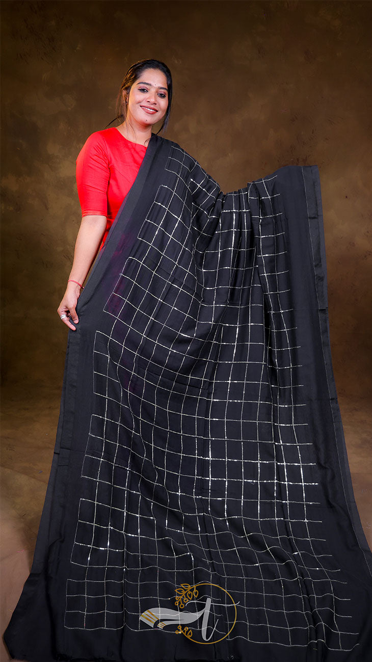 Woman wearing a black saree with white checkered pattern against a brown background