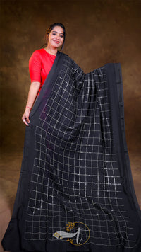 Woman wearing a black saree with white checkered pattern against a brown background