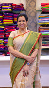 Woman in a green and beige saree standing in front of colorful fabric displays.