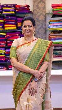Woman in a green and beige saree standing in front of colorful fabric displays.