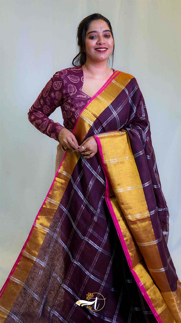 Woman wearing a traditional maroon saree with gold border against a plain background