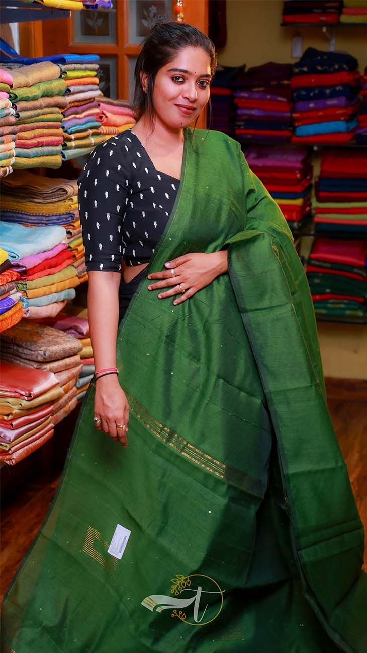 Woman wearing a green saree in front of fabric stacks
