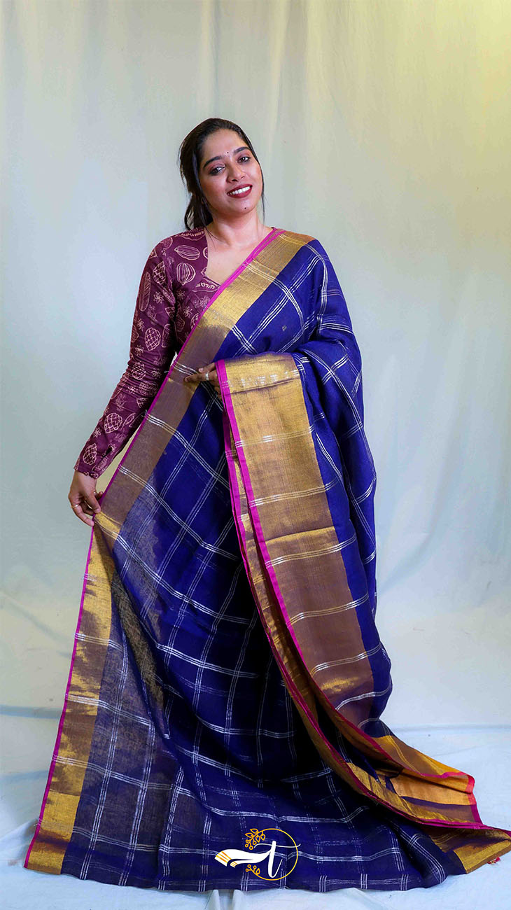 Woman wearing a traditional purple saree with a gold border against a white background