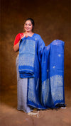 Woman holding a blue and gray saree with white patterns against a brown background