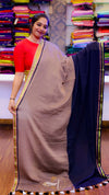 Woman holding a brown saree with a blue border in a fabric store.