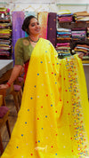 Woman holding a yellow saree with colorful polka dots and cartoon designs in a fabric store.