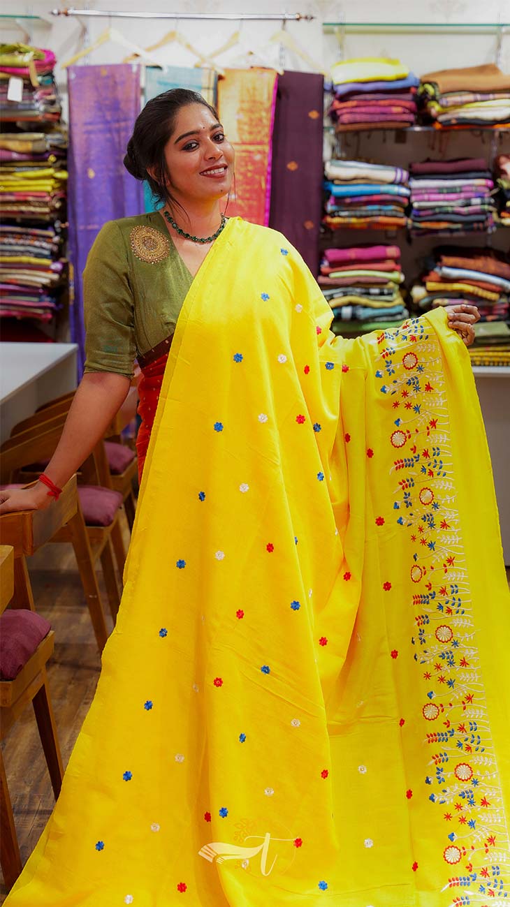 Woman holding a yellow saree with colorful polka dots and cartoon designs in a fabric store.