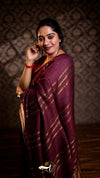 Woman in a maroon saree with gold stripes against a patterned wall.