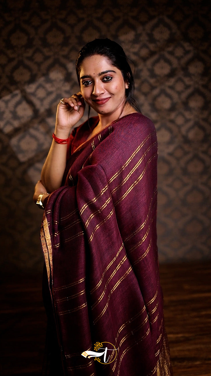 Woman in a maroon saree with gold stripes against a patterned wall.