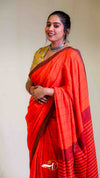 Woman wearing a bright orange saree with a yellow blouse against a plain background