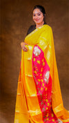 Woman wearing a bright yellow saree with a pink border against a brown background