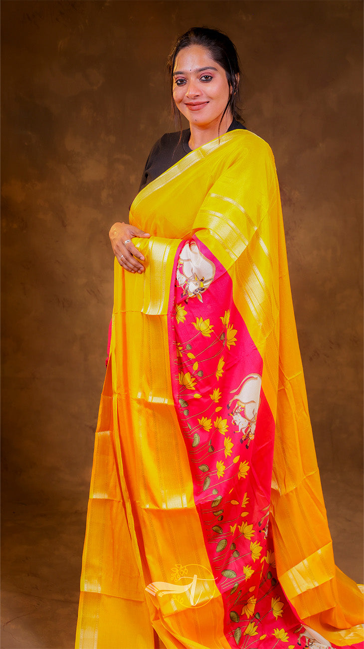 Woman wearing a bright yellow saree with a pink border against a brown background
