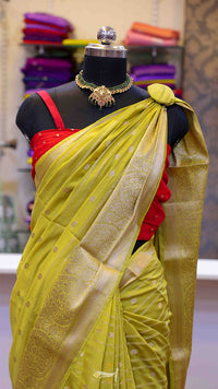 Mannequin wearing a yellow saree with a red blouse, jewelry on a mannequin head, and a blurred background of colorful fabrics.