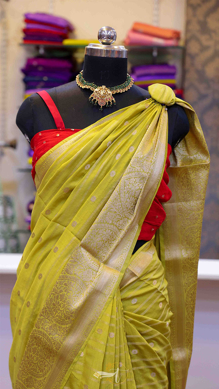 Mannequin wearing a yellow saree with a red blouse, jewelry on a mannequin head, and a blurred background of colorful fabrics.