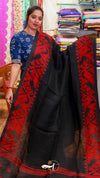 Woman wearing a black saree with red patterns in a fabric store.