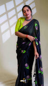 Woman wearing a black saree with green and purple patterns against a neutral background