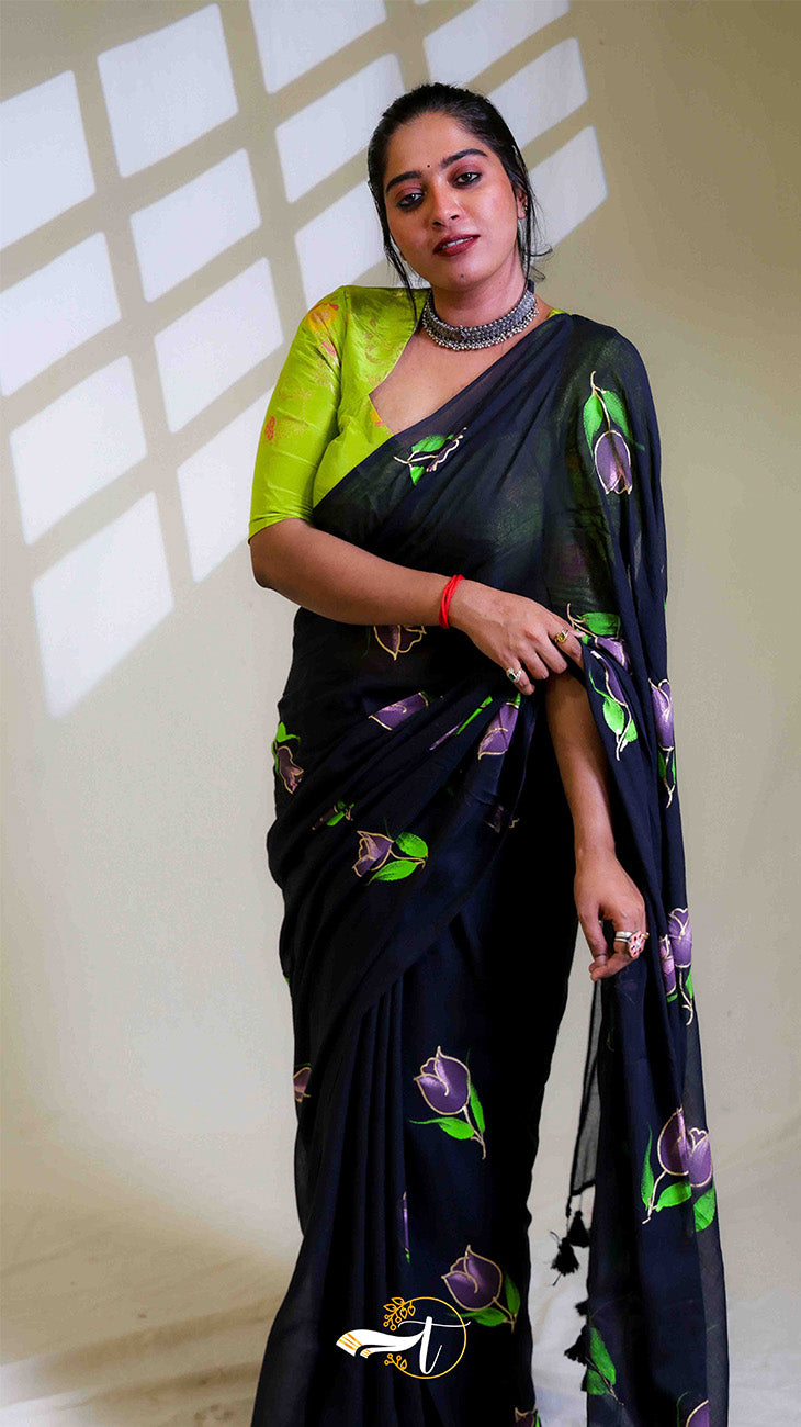 Woman wearing a black saree with green and purple patterns against a neutral background