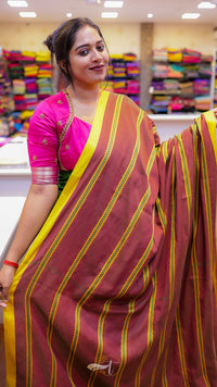 Woman wearing a pink and maroon saree with yellow stripes in a store setting.