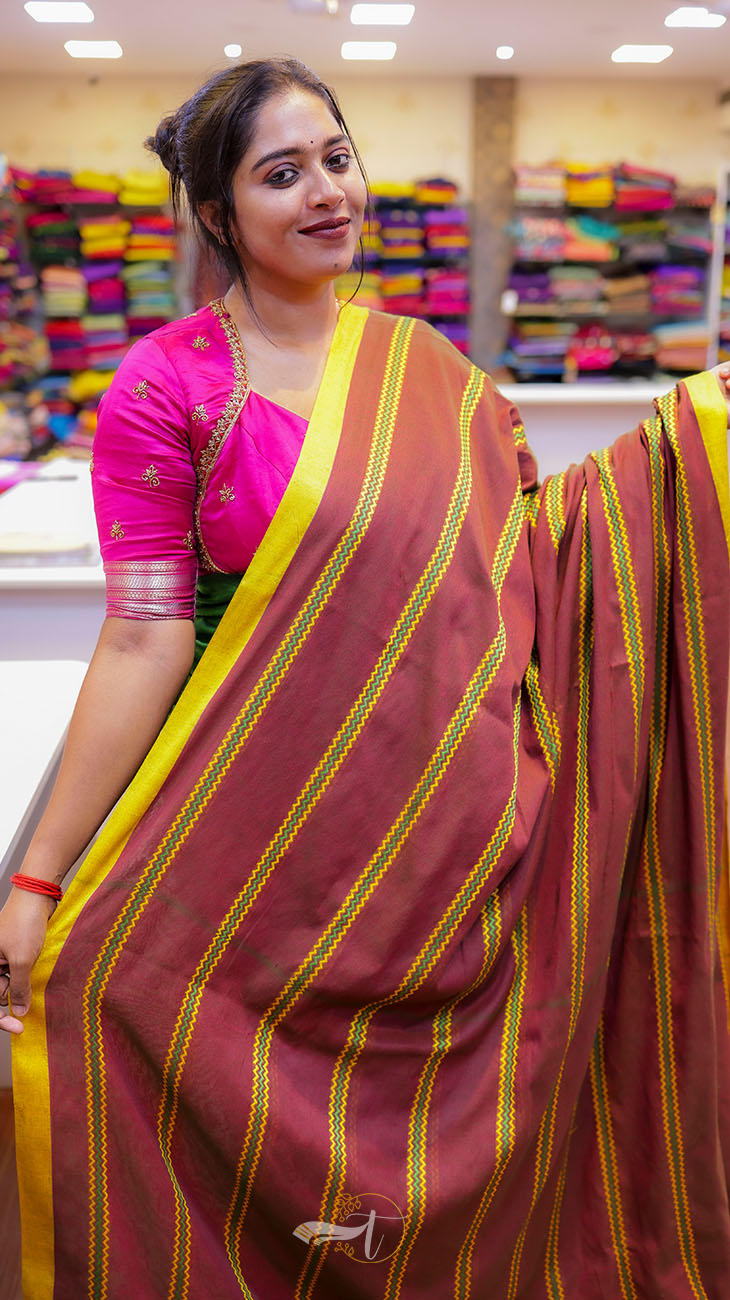 Woman wearing a pink and maroon saree with yellow stripes in a store setting.