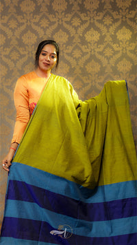 Woman holding a green and blue saree against a patterned wall.
