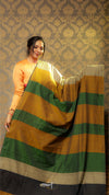 Woman holding a green and yellow saree against a patterned wall.