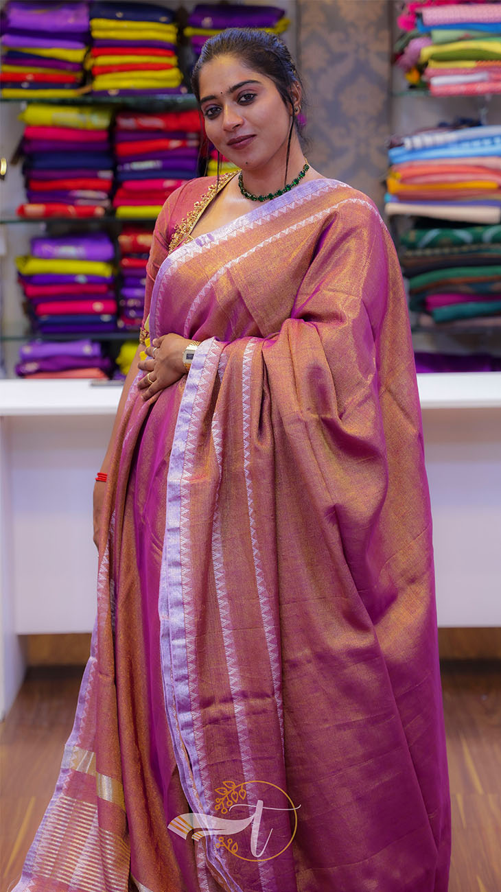 Woman wearing a pink saree with a blurred background of colorful fabrics