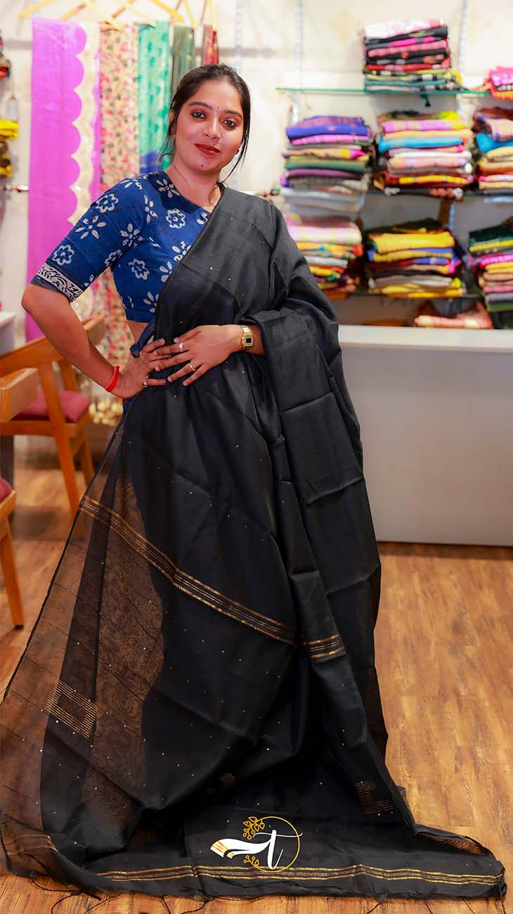 Woman wearing a black saree with a blue blouse in a fabric store.