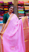 Woman wearing a pink saree with a green blouse in a store setting with colorful fabrics.