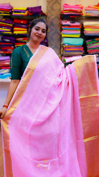 Woman wearing a pink saree with a green blouse in a store setting with colorful fabrics.