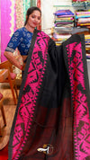 Woman holding a black saree with pink patterns in a fabric store.