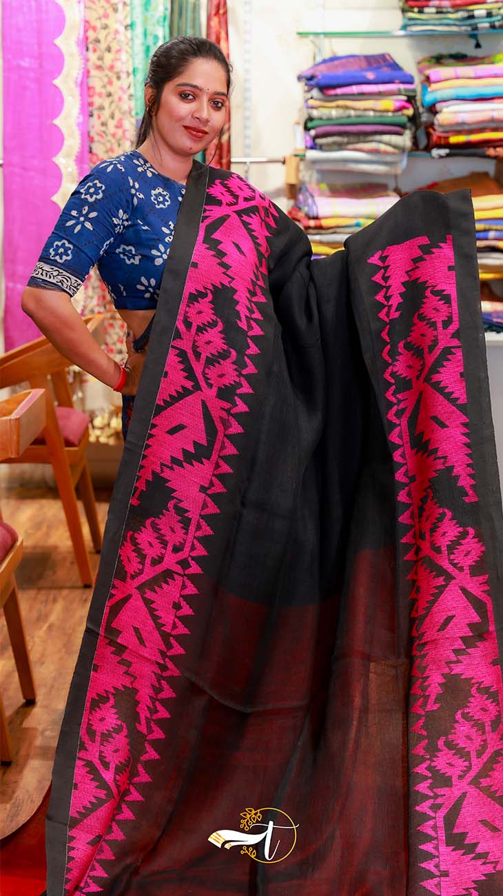 Woman holding a black saree with pink patterns in a fabric store.