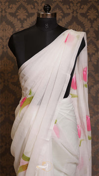 White saree with pink and green floral patterns on a mannequin against a patterned brown background