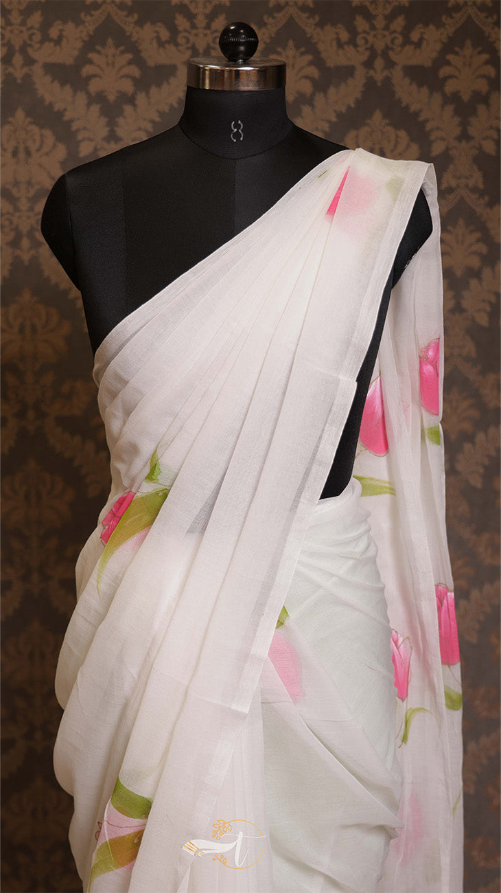 White saree with pink and green floral patterns on a mannequin against a patterned brown background