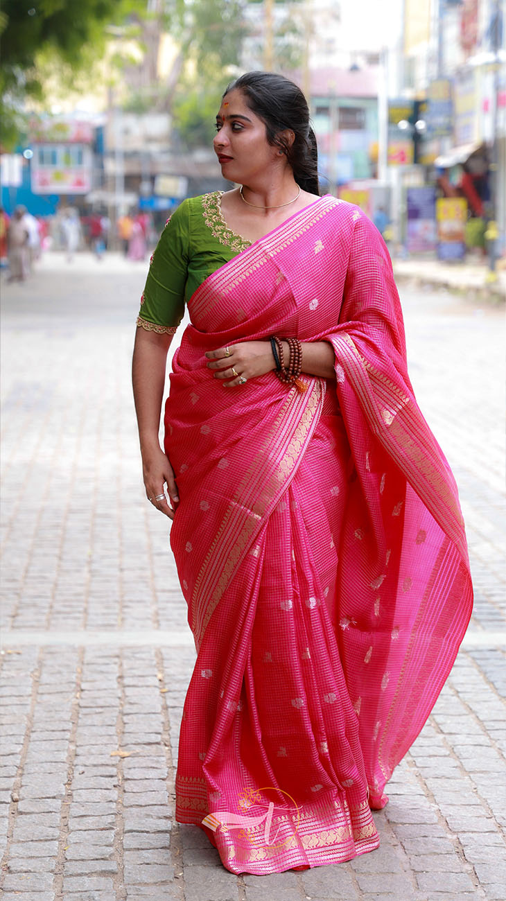 Woman wearing a pink saree with a green blouse on a street.