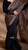 Person wearing a black saree with a patterned blouse against a brown background