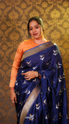 Woman wearing a blue saree with white patterns against a patterned wall.
