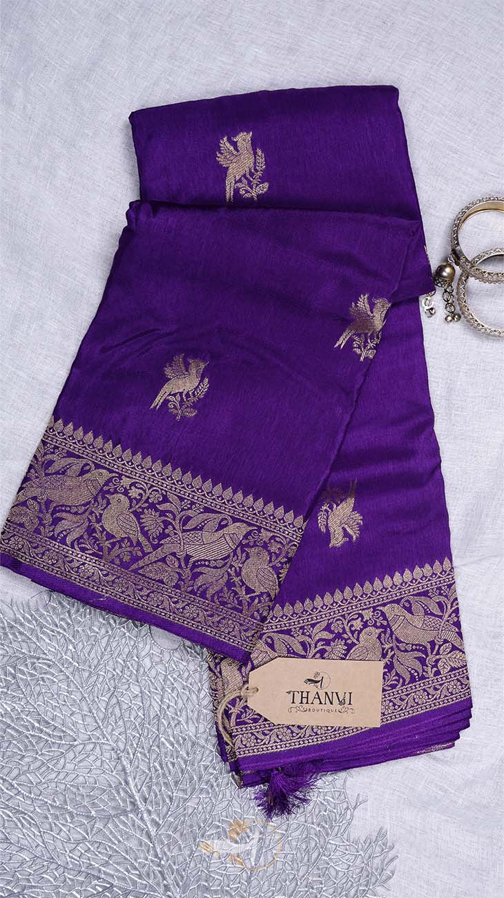 Purple saree with gold patterns on a textured gray surface, featuring the brand 'THANVI'.