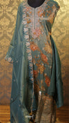 Teal embroidered outfit with floral patterns on a textured wall background