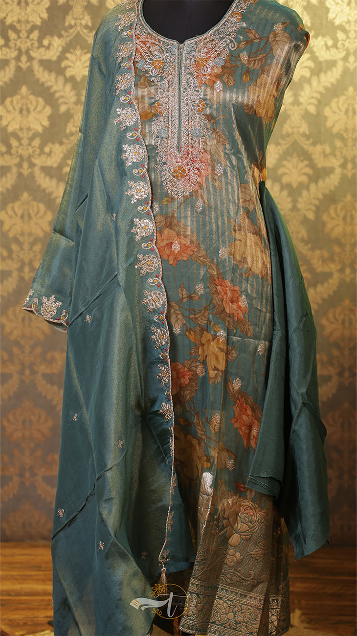 Teal embroidered outfit with floral patterns on a textured wall background