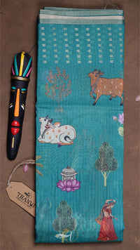 Turquoise fabric with animal and nature patterns, accompanied by a colorful pen and tag on a brown surface.