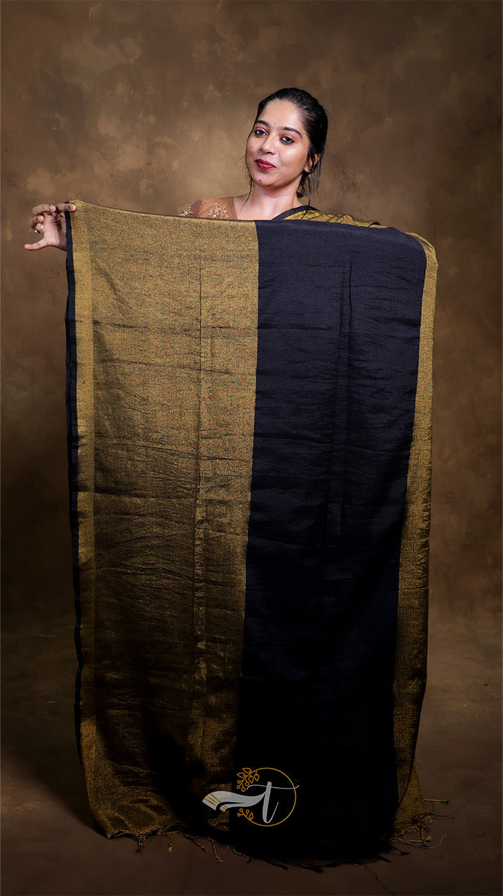 Woman holding a black and gold saree against a brown background