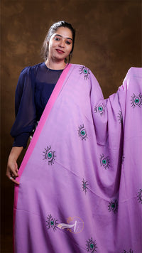 Woman wearing a purple saree with green and black patterns against a brown background